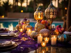 an outdoor dinner table with candles, plates and napkins next to a swimming pool