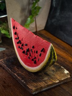 a slice of watermelon sitting on top of a wooden cutting board next to a plant