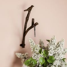 a vase filled with white flowers sitting next to a bird on a branch wall hook