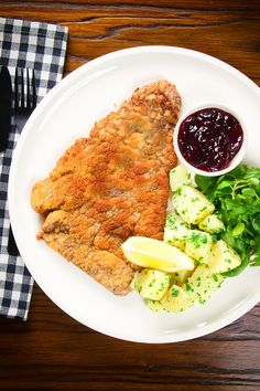 a white plate topped with meat, potatoes and salad next to a fork and knife