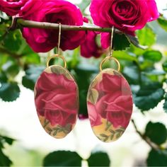 pink roses are hanging from the branch of a rose bush, with gold - plated earwires