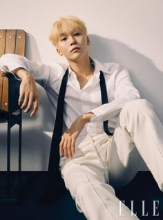 a man sitting on top of a wooden bench wearing white pants and a black tie