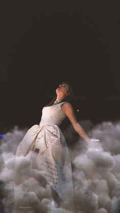 a woman in a white dress standing on top of clouds