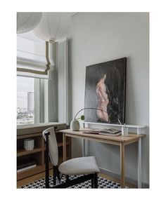 a painting hangs on the wall next to a desk with a chair in front of it