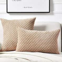 two pillows sitting on top of a white couch next to a framed poster above them