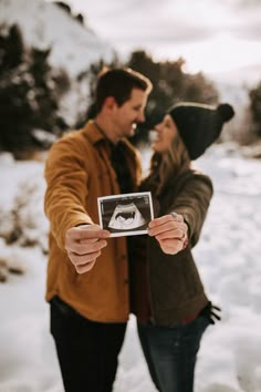 a man and woman standing in the snow holding up a polaroid frame to take a picture