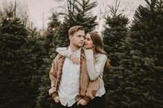 a man and woman standing next to each other in front of christmas trees