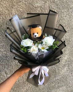 someone holding a bouquet of flowers with a teddy bear in the center and ribbon around it