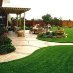 an outdoor patio and dining area with green grass, shrubs and flowers on the ground