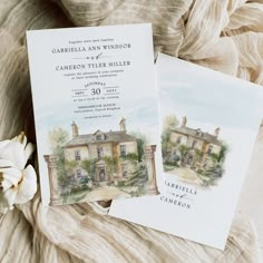 two wedding cards with watercolor paintings on them sitting on a bed next to a flower