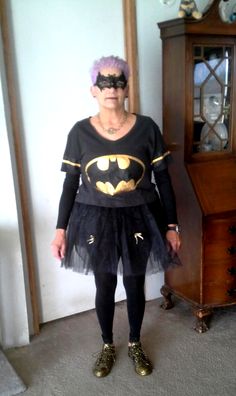 a woman wearing a batman costume standing in front of a dresser with a clock on it