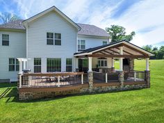 a large white house with a covered porch and grill area in front of it on a sunny day