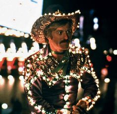 a man dressed in costume with lights around his neck and hands behind his back, standing on a city street at night