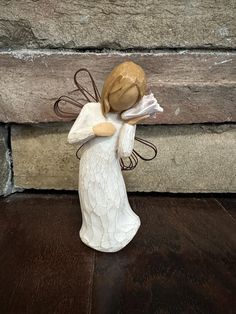 a white ceramic angel figurine sitting on top of a wooden floor next to a stone wall