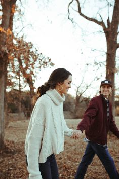 a man and woman holding hands walking through the woods