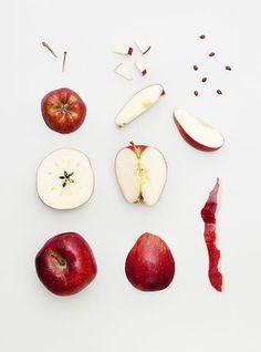 an apple sliced in half with other apples and spices scattered around it on a white surface