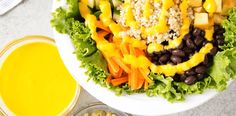 a salad with black beans, carrots and corn on it next to a glass of orange juice