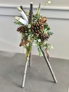 two sticks with pine cones and flowers in them on top of a table next to a wall