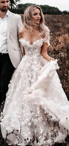 a man and woman are walking through the field together wearing wedding dresses with flowers on them