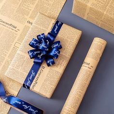 two rolls of paper with blue ribbon on top of each other next to a rolled up newspaper