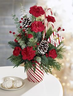 a red and white vase filled with flowers on top of a table next to a plate