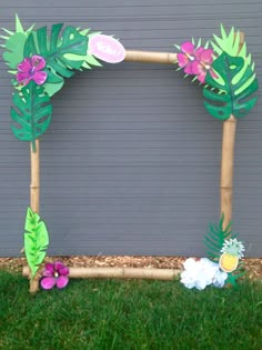 a photo frame made out of paper with flowers and palm leaves on the grass next to a garage door