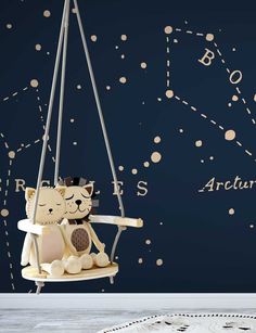 a teddy bear sitting on a swing in front of a wall with stars and constellations