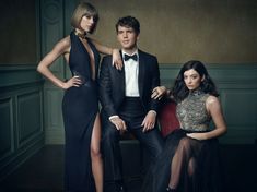 two women and a man in formal wear posing for a photo with their legs crossed