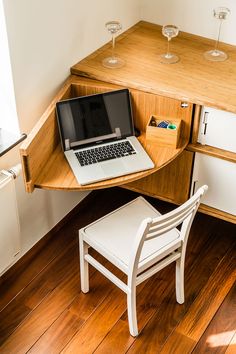 an open laptop computer sitting on top of a wooden desk next to a white chair