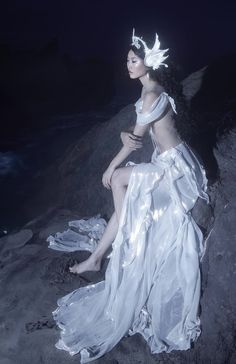 a woman sitting on top of a rock wearing a white dress and headdress