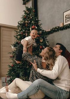 a man, woman and baby are sitting in front of a christmas tree