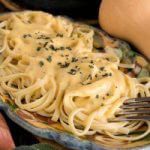 a plate full of pasta with cheese sauce and herbs on the top is being held by a fork