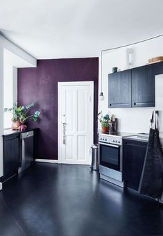 an empty kitchen with purple walls and white trim on the door, black flooring and stainless steel appliances