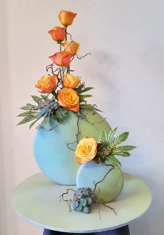 two blue vases with orange roses and succulents on top of a table