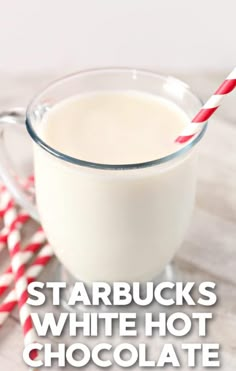 a glass cup filled with white hot chocolate next to two red and white striped straws