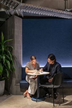 two people are sitting at a table in front of a blue wall and planter