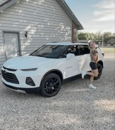 a woman standing next to a white chevrolet suv in front of a house with her hand on the door handle