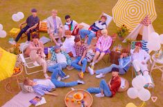 a group of people sitting on top of a grass covered field next to umbrellas