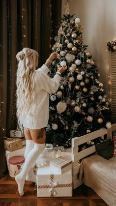 a woman standing in front of a christmas tree with presents on the floor next to it