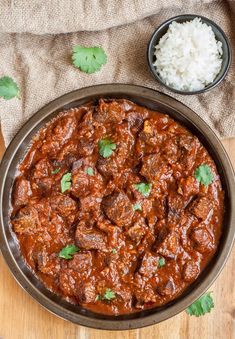 a pan filled with meat and rice on top of a wooden table next to a spoon