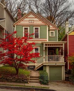 a tree with red leaves is in front of a green two - story house on a street corner