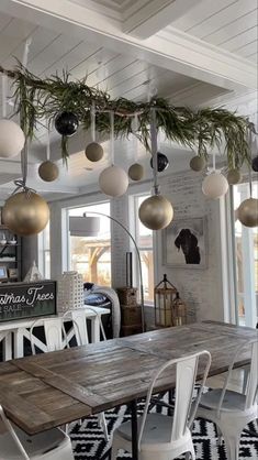 a dining room table with white chairs and hanging ornaments on the ceiling in front of a large window