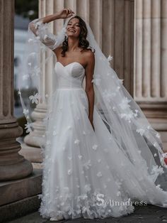 a woman wearing a wedding dress with flowers on the skirt and veil, standing in front of columns