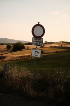 two street signs sitting on top of a grass covered field next to a lush green hillside