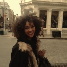 a woman standing in front of a building on a city street smiling at the camera