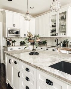 a kitchen with white cabinets and marble counter tops, an island in front of the sink