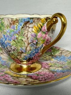 an ornate cup and saucer with gold trimmings on the rim, decorated with colorful flowers