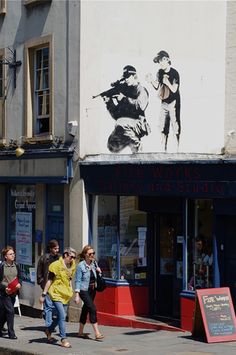 people walking on the sidewalk in front of shops and buildings with an advertisement painted on the building