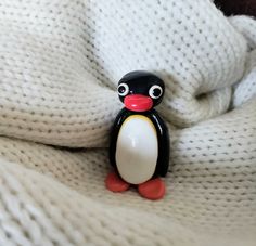 a penguin figurine sitting on top of a white blanket with eyes wide open