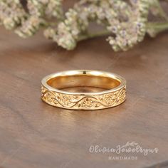 a yellow gold wedding band with filigrees on the side and flowers in the background